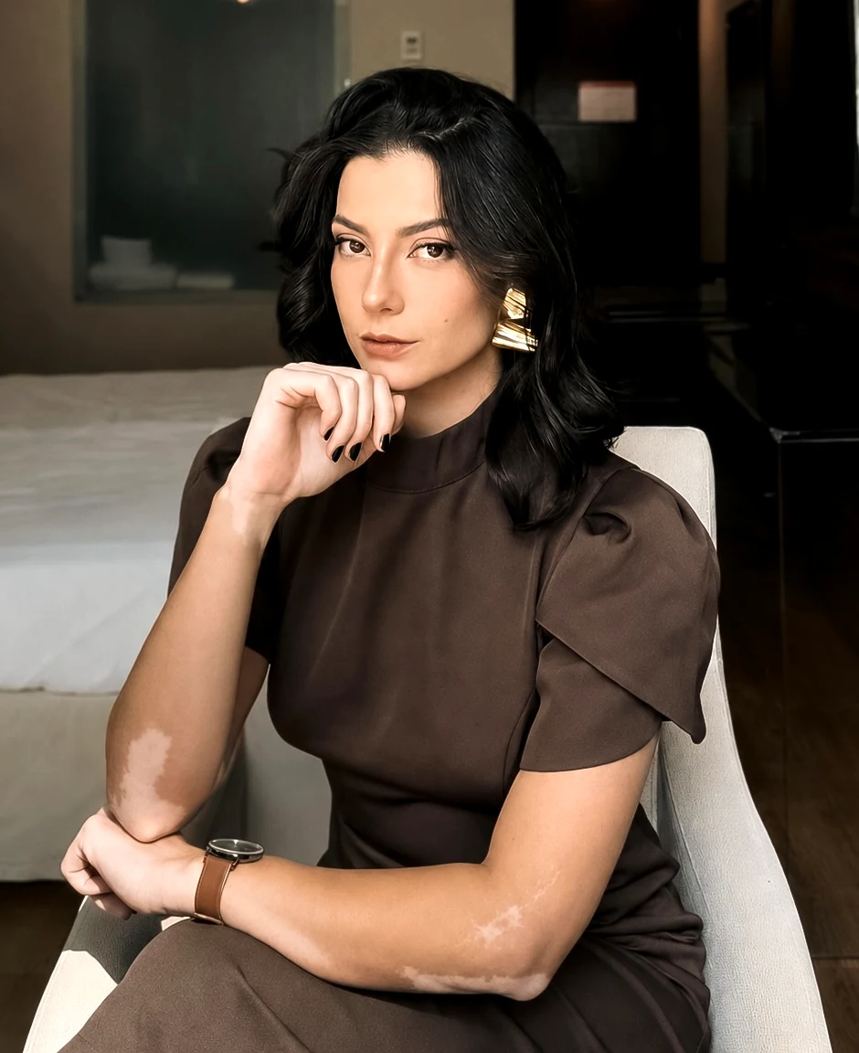 Katharina Zaparoli sentada em poltrona, vestido marrom, com olhar direto para a câmera